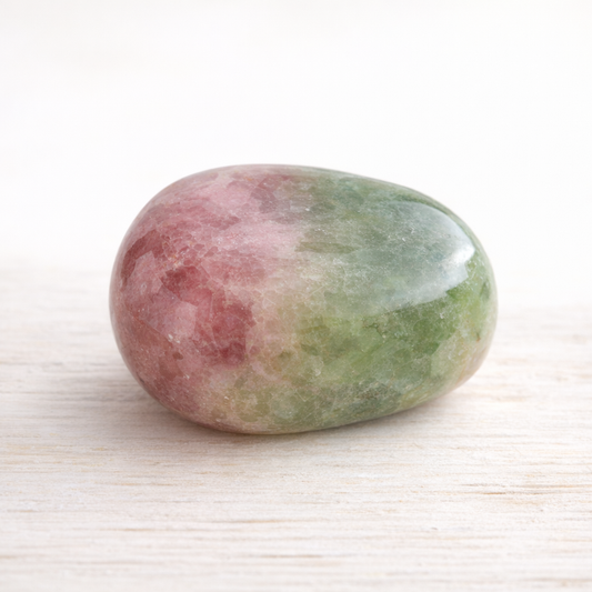 Pummeliger bunter Turmalin-Trommelstein mit rosa und grünen Zonen auf hellem Holz